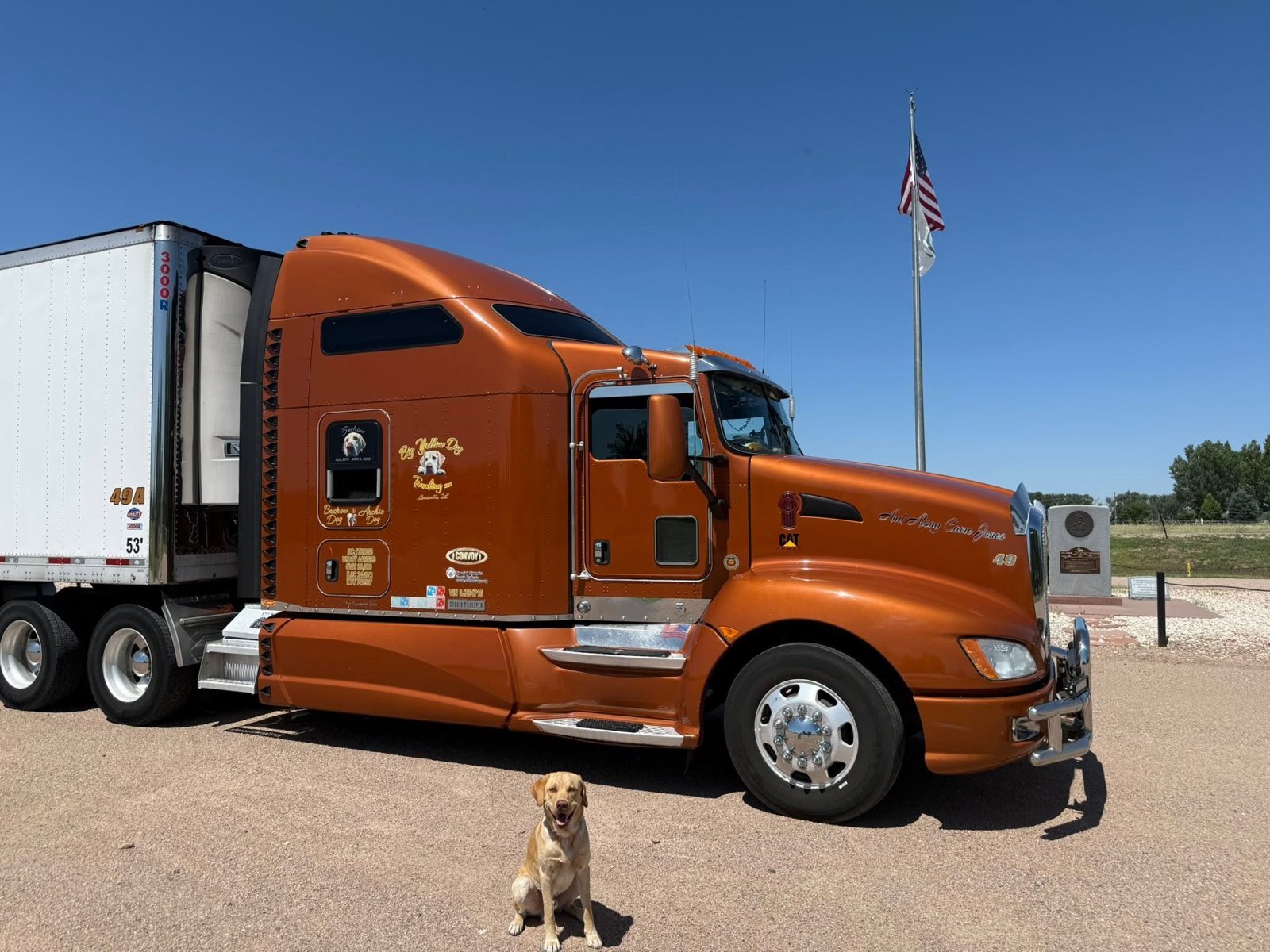 Front three-quarter view of the orange semi by an American flag with Archie sitting out front